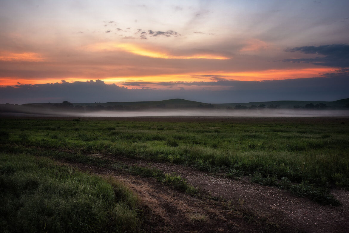 Landscape showing gravel road and low lying fog with hills in background at dawn.